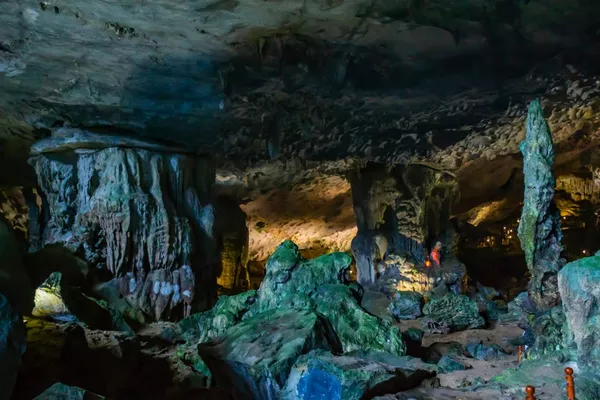 Dark limestone cave interior with glowing rock formations and stalactites, with a few visitors standing among the shadows