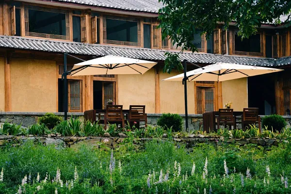 Lodge courtyard in Shangri-La with green lawns, stone edging, and umbrella-shaded seating outside traditional country-style buildings