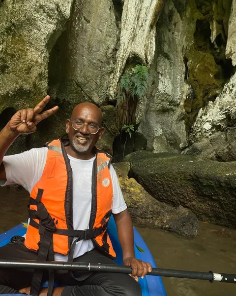 Selva, Langkawi naturalist guide, smiles with a peace sign in an orange life jacket while kayaking inside a rocky cave