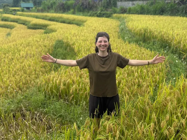 Smiling traveller with arms out in lush green and golden rice terraces near Ha Giang during the Ha Giang loop
