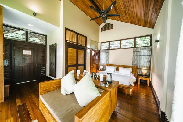 Borneo Rainforest Lodge bedroom in Danum Valley featuring two beds, timber interior, and a seating area with drinks on a bedside table