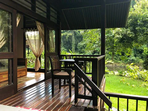 Open-air veranda of Borneo Rainforest Lodge in Danum Valley, with wooden seats and curtains overlooking a lush rainforest garden