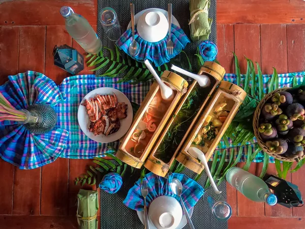 Jungle dining table with grilled meat, vegetables and glasses arranged on a wooden floor at Anurak Lodge in Khao Sok National Park.