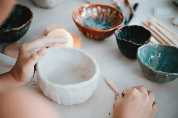 Hands shaping a white clay bowl on a studio workbench during guided pottery workshops in Singapore