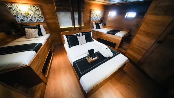 Angelica Liveaboard phinisi suite with a double bed, wooden doors and headboards, and a view into the cabin layout
