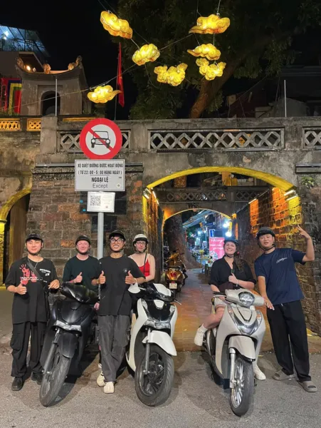 Small group on motorbikes posing outside a lit tunnel gate at night in Hanoi for a Zero‑Tourist food adventure