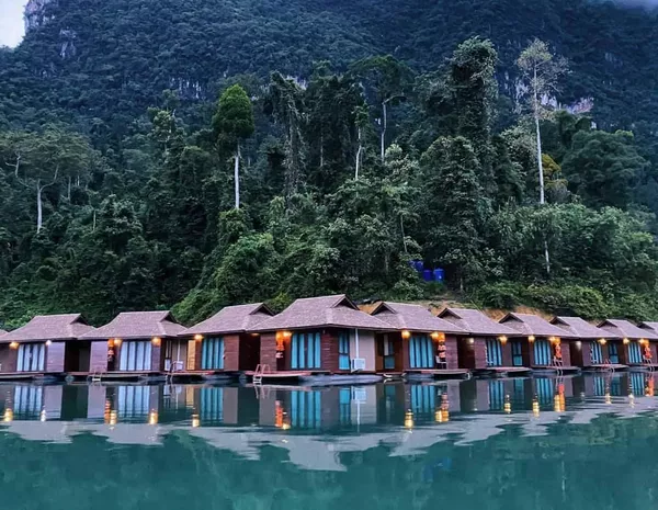 黄昏时分,静谧的湖面倒映着一排豪华木质露营小屋,背后是茂密丛林山峦——考索国家公园