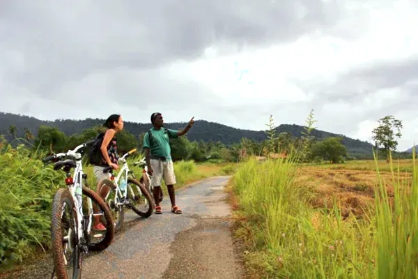Cyclists ride along a quiet country road in Langkawi with mountains and greenery ahead, part of villages, markets and jetty cycling