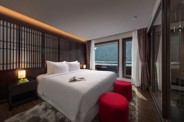 Oasis Bay Party Cruiser stateroom with double bed, red seating and large window framing Halong Bay seascapes