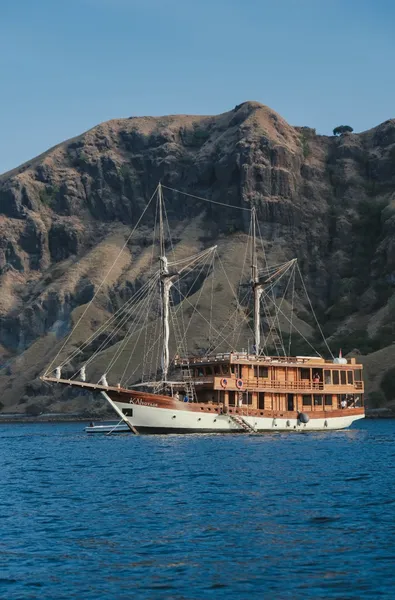 Wooden phinisi sailing on bright blue water beside rugged Komodo hills during a shared 3D2N cruise to Komodo Island