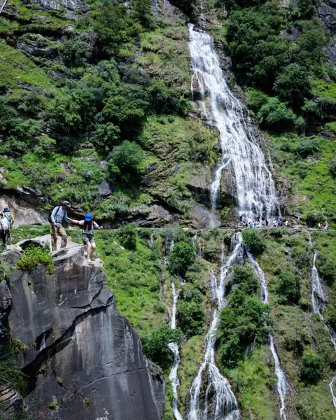 Waterfall plunging beside lush cliffs as hikers pause on the Tiger Leaping Gorge high trail near Lijiang, Yunnan