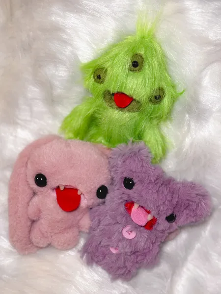 Ugly-cute plush keychain characters on white faux fur, including a bright green creature, from Avant-Garde Art Space workshops in Singapore