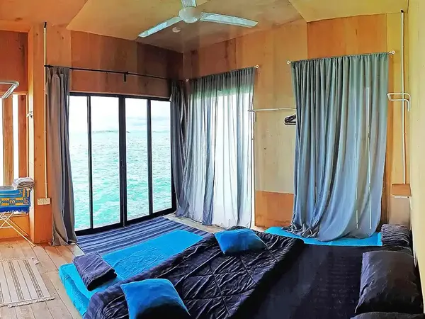 Sea lodge room in Semporna with a double bed, blue bedding, and large ocean-facing windows with curtains