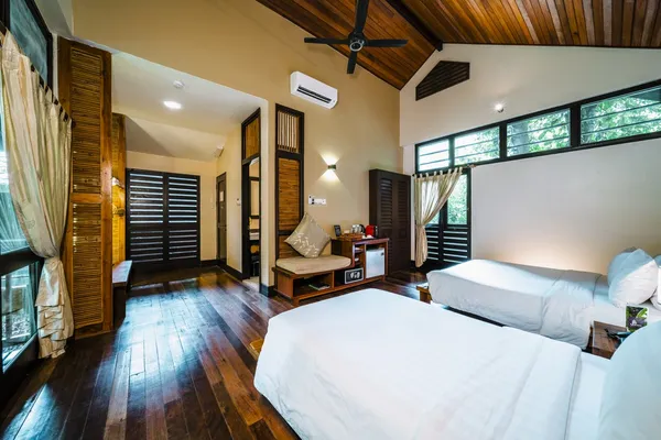 Borneo Rainforest Lodge guest bedroom in Danum Valley with double bed, ceiling fan, polished timber floors, and large rainforest windows