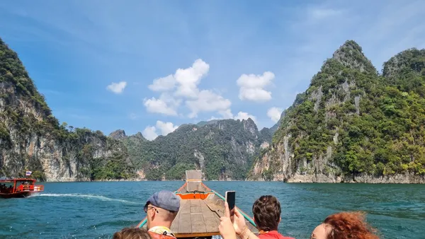 Travellers on a boat cruising calm water with limestone karsts under blue skies in Khao Sok National Park