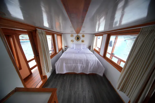 Wooden boat cabin with double bed centred and curtains on both sides, ocean visible through the windows on a 3D2N Komodo trip Labuan Bajo