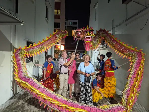 People posing inside a colourful dragon-dance installation with painted panels and lanterns on a narrow Geylang street