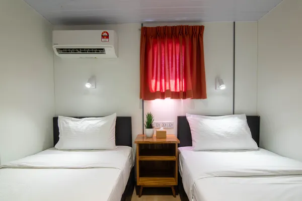 Twin beds in a Seaventures Dive Rig cabin, each with crisp white linens, a bedside table and red curtains