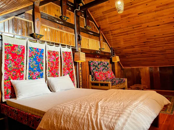 Red Dao homestay bedroom during a 2D1N stay, with a carved wooden double bed and bright brocade textiles, in Sapa