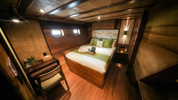 Spacious luxe phinisi cabin with bed, side table and reading chair for the 3D2N Komodo cruise, sunset BBQ and jacuzzi in Labuan Bajo
