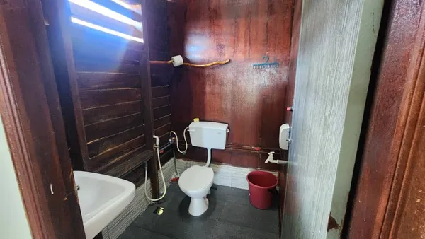 Toilet and wash area in a bathroom at Luma Selakan sea lodge in Semporna, with a shower screen and red bucket