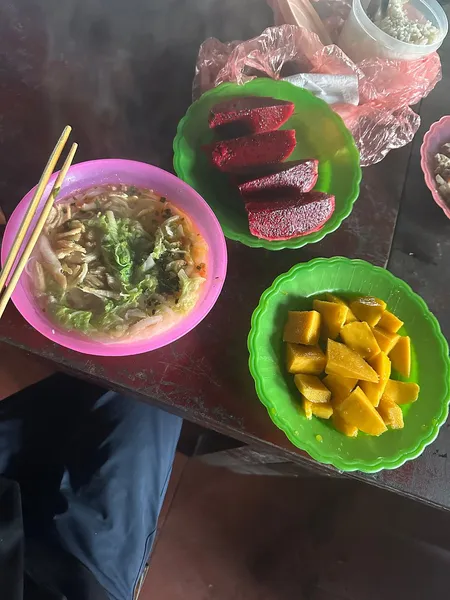 Trail lunch during a 1-day Fansipan eco trek in Sapa: noodles in a pink bowl and mango cubes on a green plate