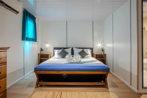 Seaventures Dive Rig cabin with a neatly made double bed, bedside drawers and wall windows, for an offshore rig stay in Semporna