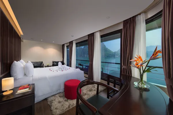 White turndown bed and window curtains framing Halong Bay views inside an Oasis Bay Party Cruise cabin