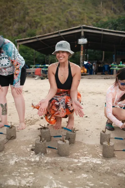 People kneeling on a sandy beach placing cement coral plugs under cover as part of the Rinca Coral Nursery Program, Labuan Bajo