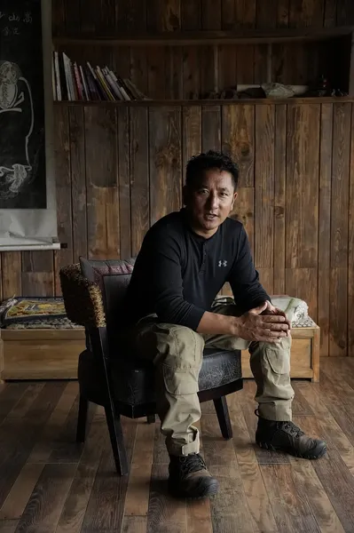 Khampa Caravan host seated in a rustic wooden room at a Tibetan home in Shangri-La, during a cultural experience