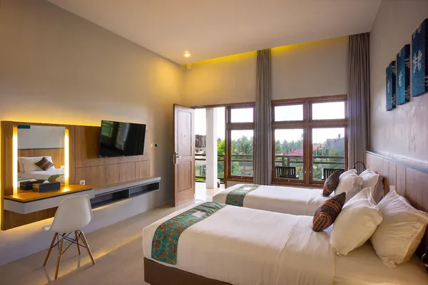 Kamar tidur tamu yang terang oleh sinar matahari dengan tempat tidur double, TV, dan pintu balkon, interior akomodasi untuk itinerary 5H4M Bromo ke Ijen