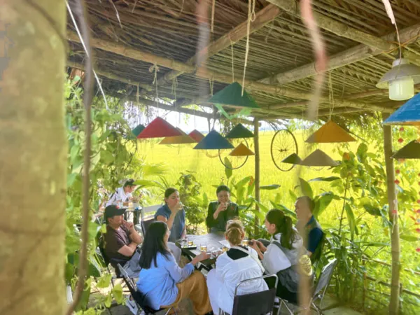 Sekelompok pelancong menikmati hidangan bersama di bawah atap rumbia di Hoi An, Vietnam, dalam tur sorotan berpemandu