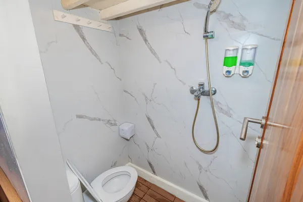 Marble-tiled bathroom on a Komodo boat trip with toilet, handheld shower and wall dispensers for the 3D2N stay in Labuan Bajo