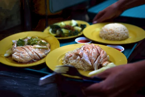 Server’s hands placing yellow plates of hawker dishes on a Singapore table, captured mid-service during a hidden hawker stories tour