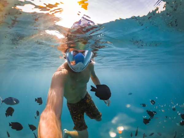 Seorang penyelam skuba di bawah permukaan berhampiran terumbu pulau Semporna, dikelilingi ikan karang semasa menyelam bersama Bigfin Divers