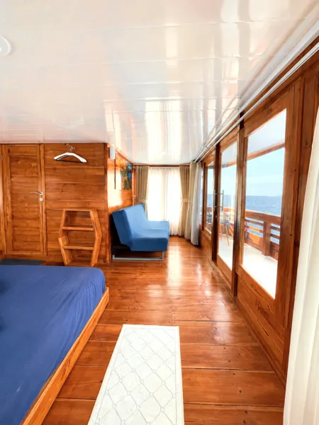 Wooden phinisi cabin lounge with sofa, sliding doors and ocean-view windows on a 3D2N shared cruise from Labuan Bajo, Komodo Island