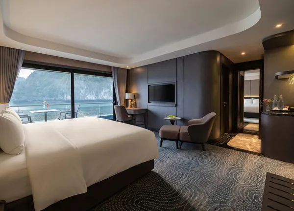 Kamar Tulip Cruise dengan tempat tidur besar dan kursi santai, menghadap Teluk Lan Ha melalui jendela dari lantai hingga langit-langit