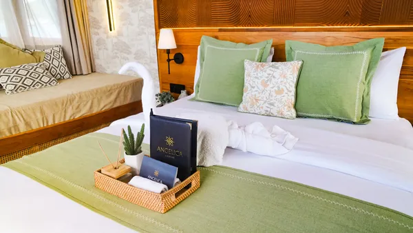 Green-and-white cabin bed with decorative pillows and a bedside welcome tray in a phinisi suite, on a Labuan Bajo cruise