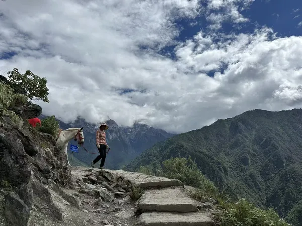 Hikers trekking the Tiger Leaping Gorge high trail on rocky steps with clouded mountain views in Lijiang, China