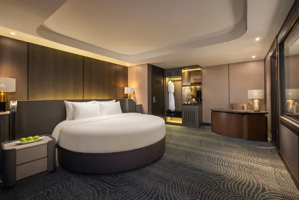 Elegant Doris Cruise cabin with neatly made bed and minibar nook, showing calm water scenery over Halong Bay through glass