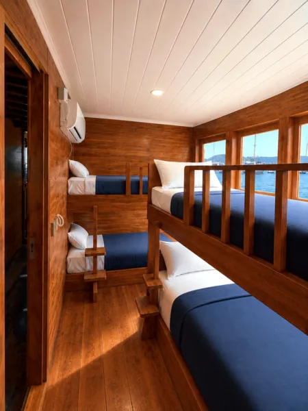Wooden phinisi cabin bunks with blue bedding and sea view through wooden rails, on a shared Komodo 3D2N cruise in Labuan Bajo