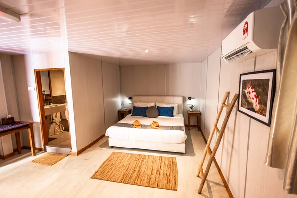 Air-conditioned cabin bedroom with double bed, wooden bedside unit and framed wall art on Seaventures Dive Rig offshore stay in Semporna