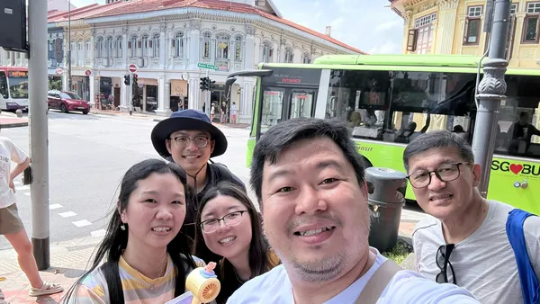 Group smiling at a Singapore bus stop in Katong-Joo Chiat during a real-life Monopoly team challenge, team building Singapore