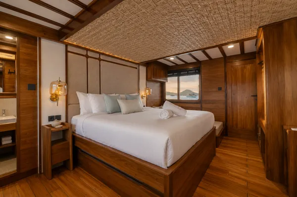 Travass Life phinisi cabin interior with a large double bed and soft lighting for a Komodo shared trip, Labuan Bajo