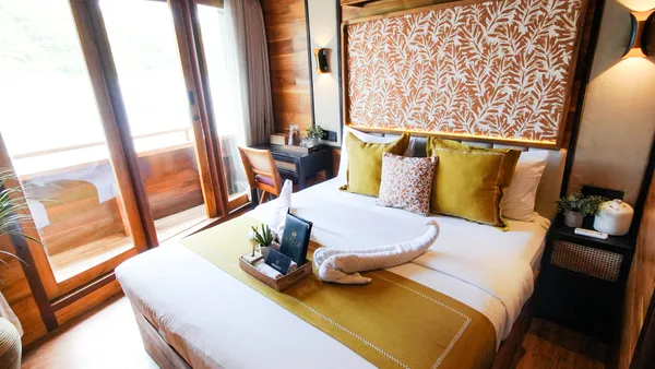 Luxurious phinisi cruise cabin by Angelica Liveaboard with a made-up bed and balcony doors for sunset views in Labuan Bajo