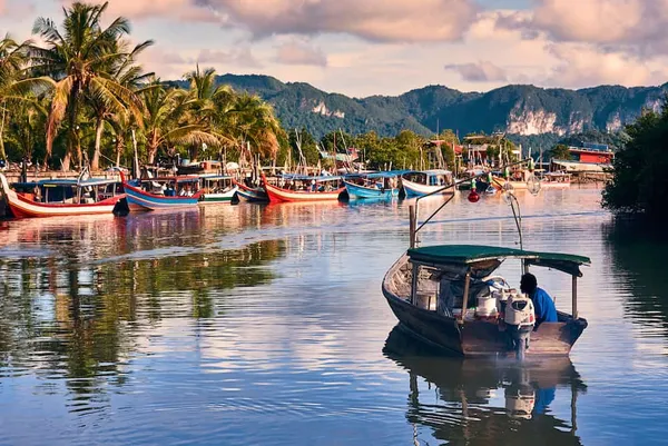 Moored boats at a Langkawi jetty with calm reflections during a cycling day with Dev's Adventure Tours, by mountain scenery