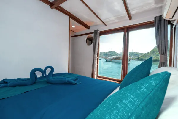 Phinisi cabin bed with folded-towel decoration beside large windows, for a 3D2N adventure to Komodo Island