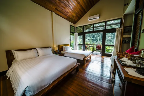 Borneo Rainforest Lodge room in Danum Valley with two beds, big window doors to a balcony, and a wooden writing desk