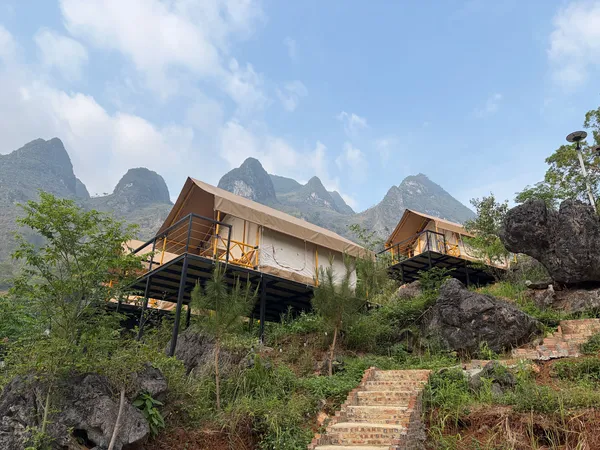 Glamping tents on raised platforms set among rocks and greenery with mountain peaks behind, camping in Ha Giang during the Ha Giang loop