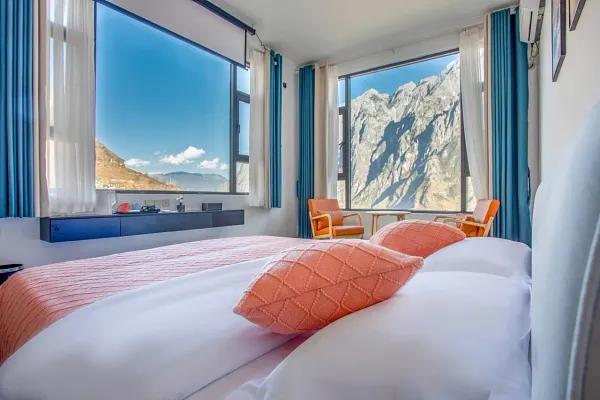 The Bivou Lijiang guest room with a double bed and orange cushions, floor-to-ceiling window framing dramatic mountain peaks